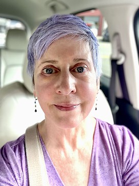 Woman with a lavender pixie cut with visible swelling around the eye smiling.