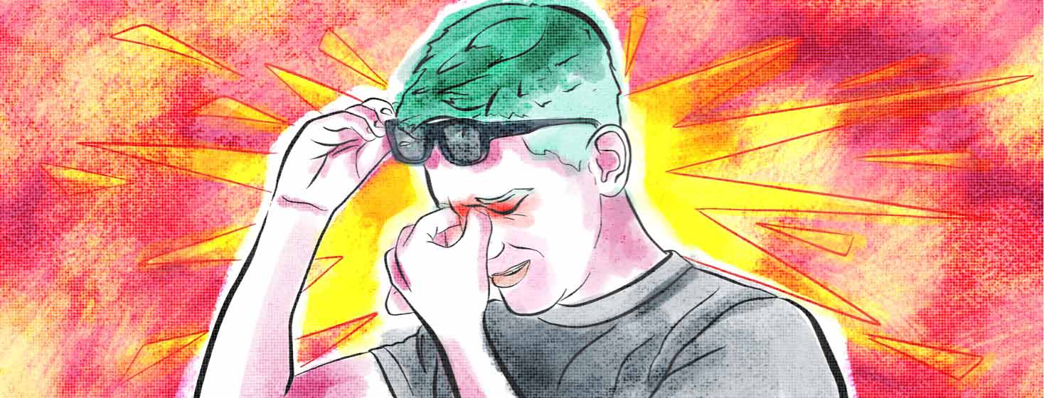 A man removes his glasses and grabs at his itching eyes that appear red and blotchy.