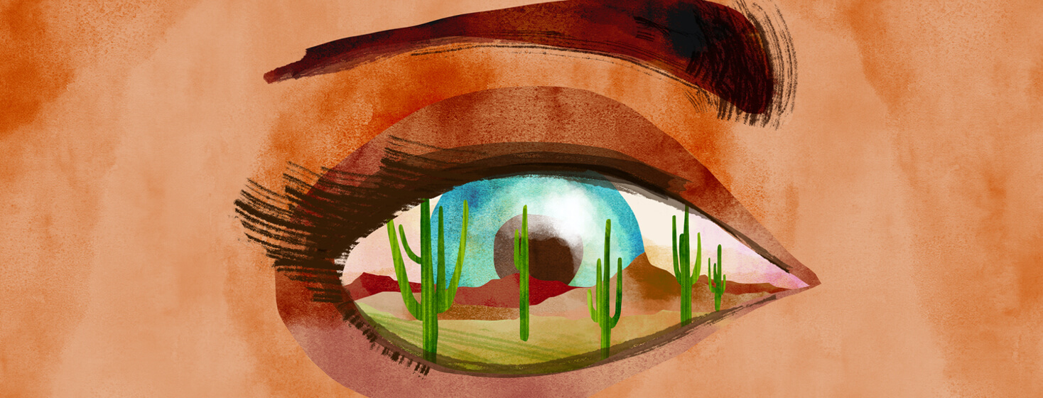 A close up of a desert scene with cacti is reflected in a blue eye.